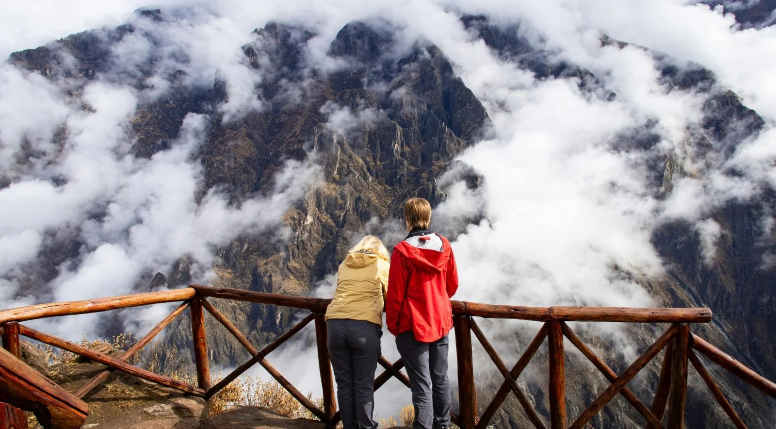 Visitor at a wooden viewpoint railing above cloud-filled canyon slopes